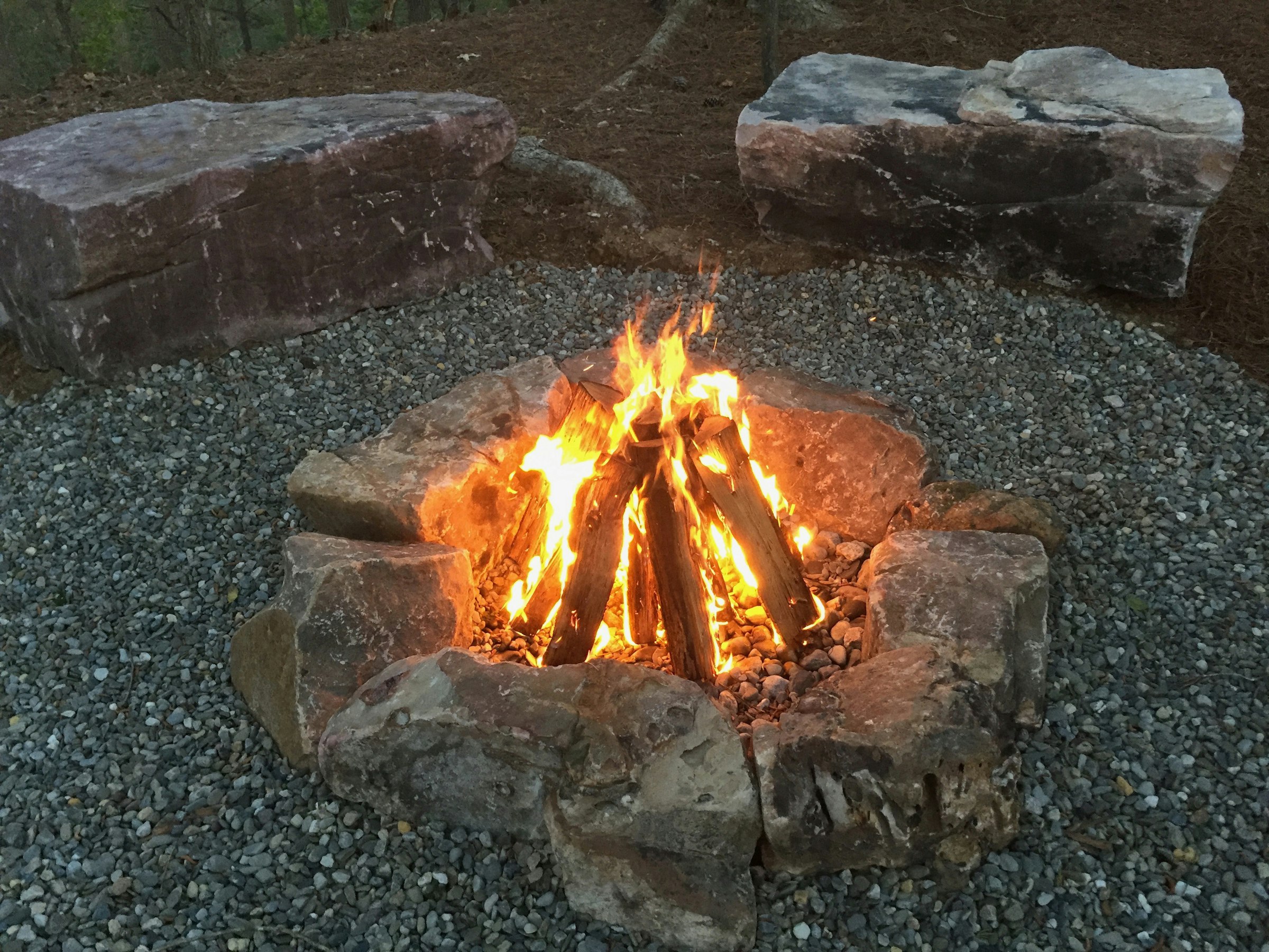 Natural stone fire pit with flames, surrounded by boulders on gravel