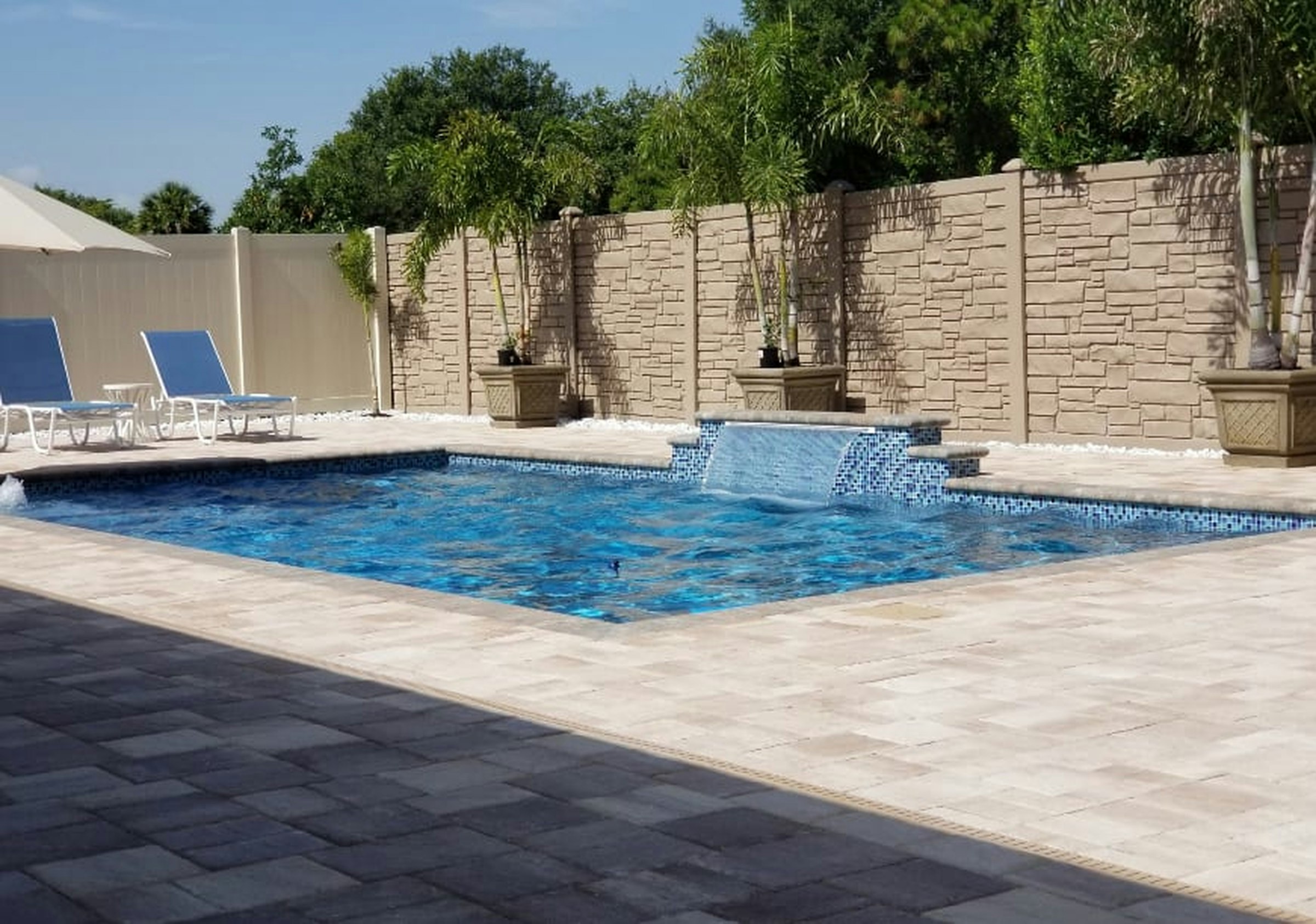 Light paver pool deck with a sheer water feature along a stone-look wall