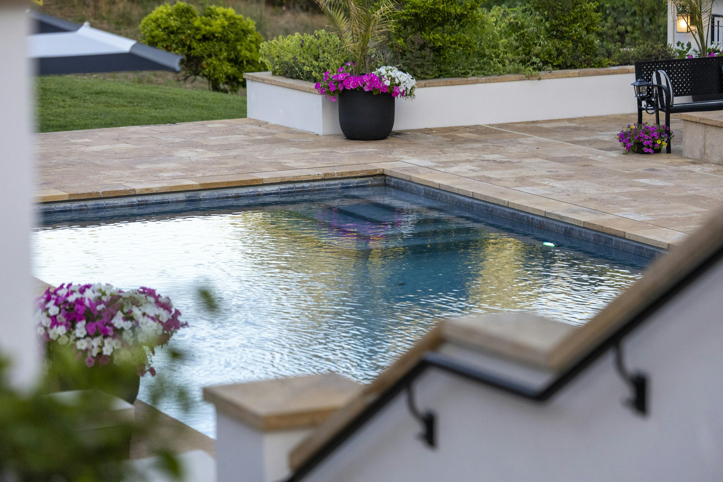 Travertine-look pool deck and coping with potted flowers