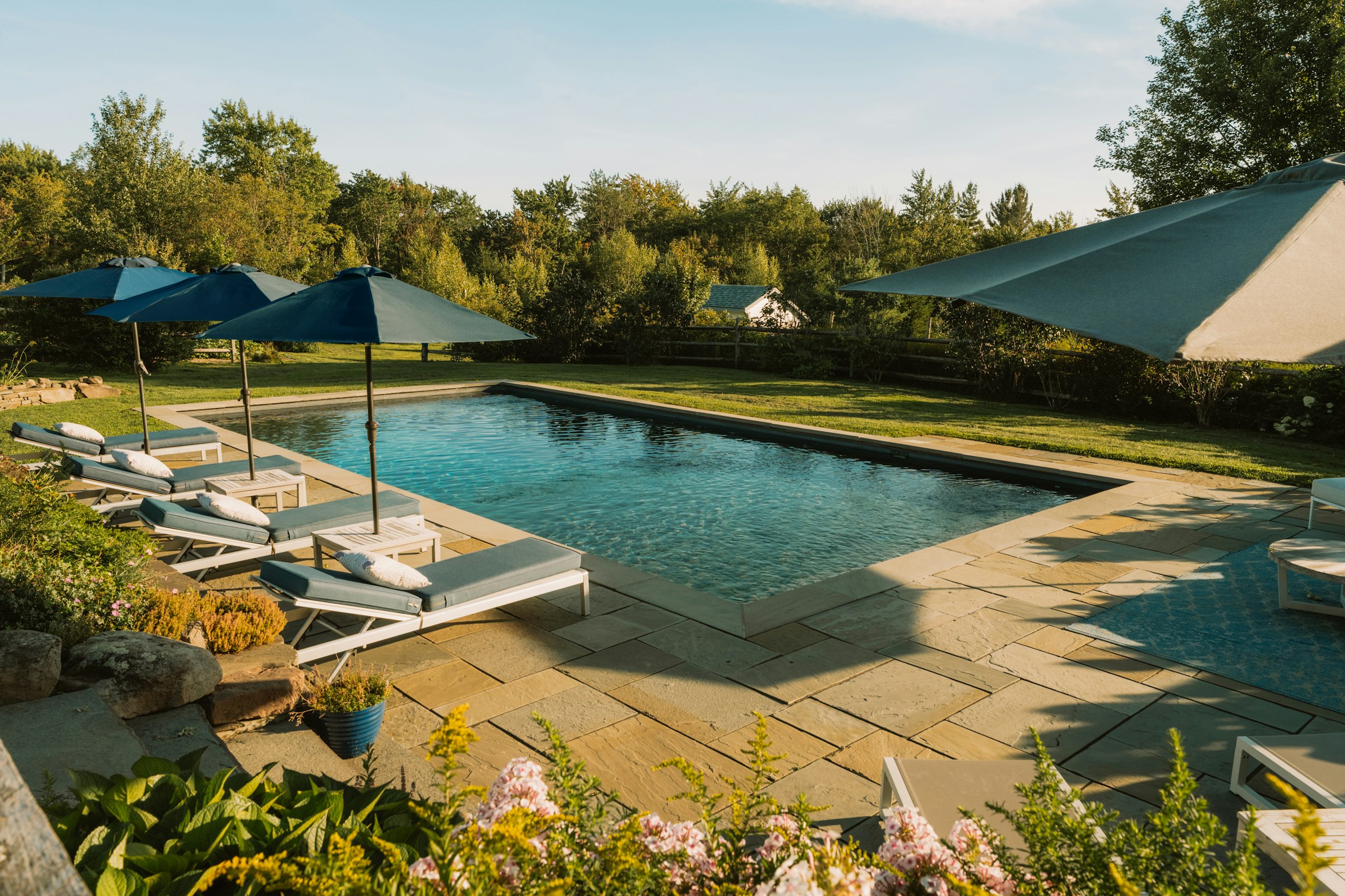 Stone pool deck with loungers and shade umbrellas beside a rectangular pool