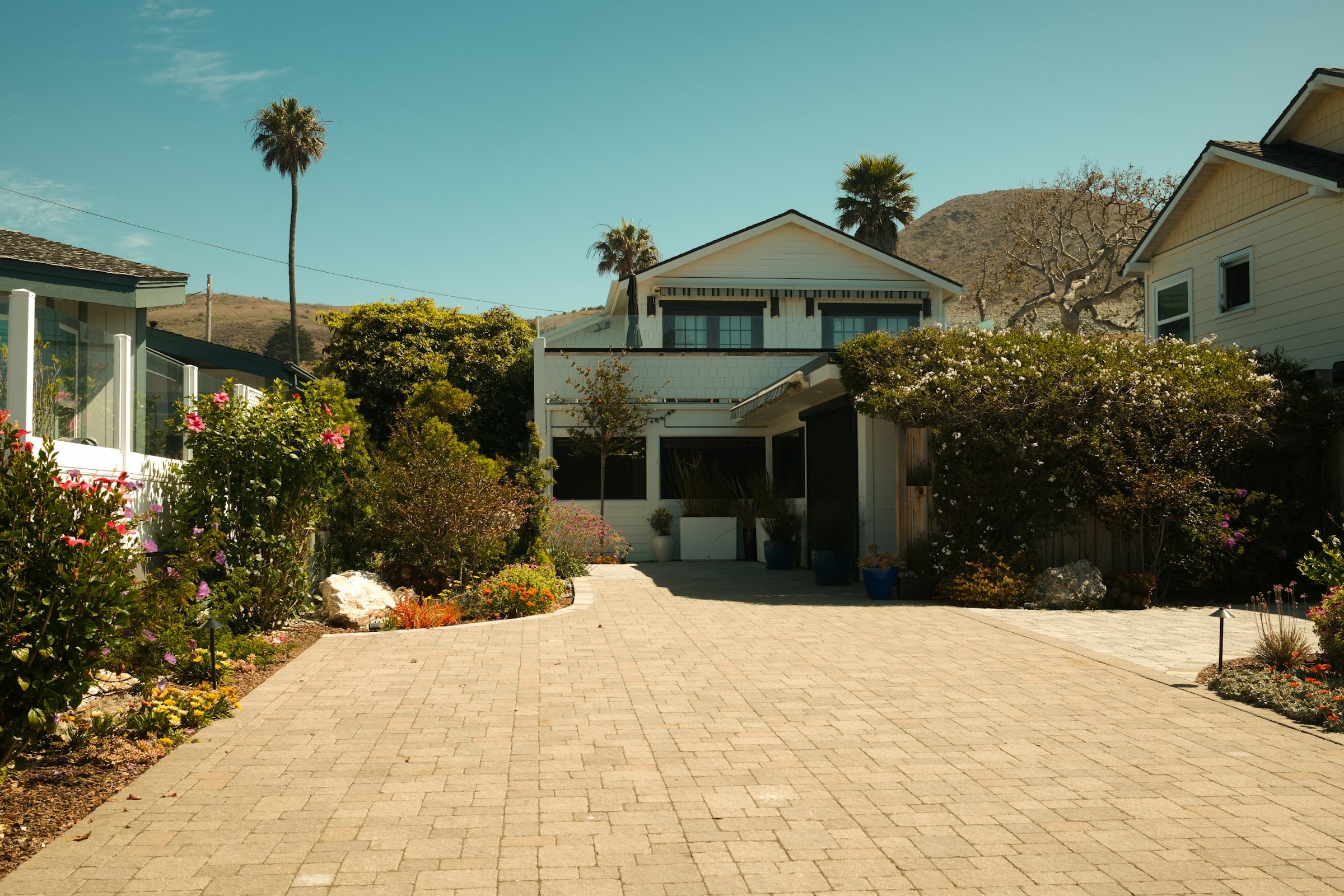 Wide light paver driveway and entry court in front of a two story home with palms