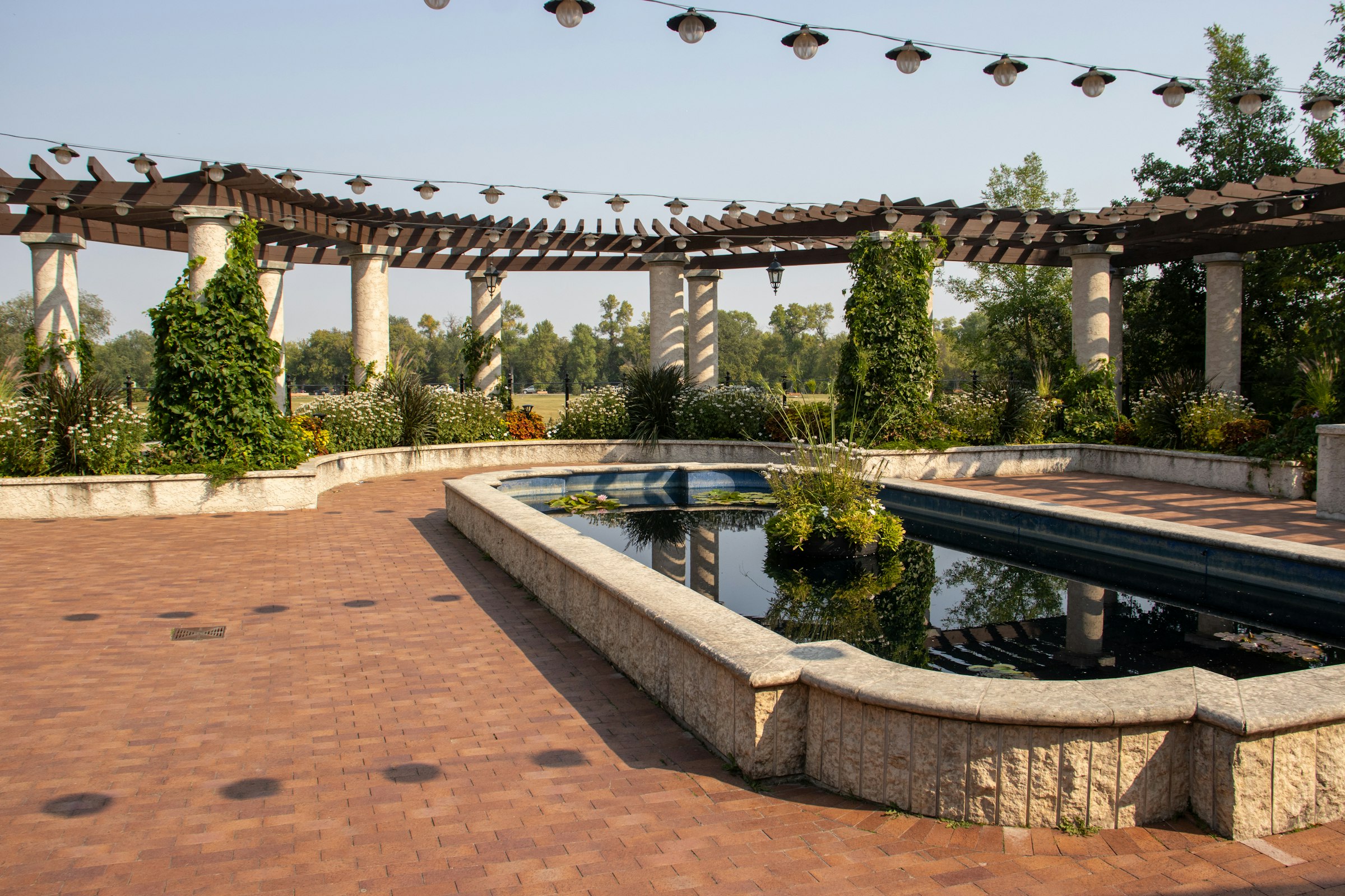 Red brick paver terrace around a raised pond under a white pergola